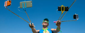 UGC Bunt gekleideter Mann hält mehrer Handys mit Selfiestick und fotografiert sich.